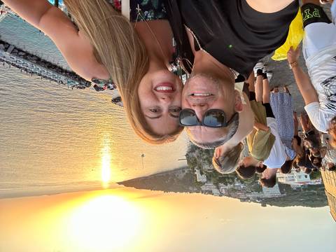 Couple posing with a sunset over the sea in the background.