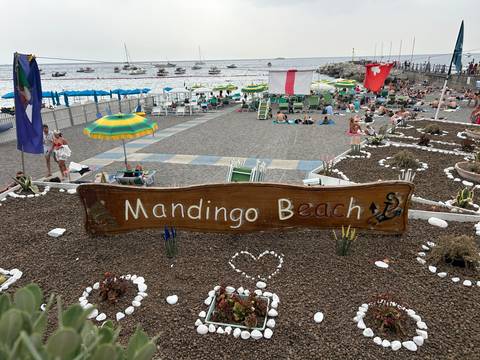 View of a beach with umbrellas and a wooden sign reading 'Mandingo Beach'.