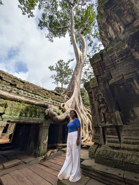 Woman posing beside roots of large tree growing among temple ruins.