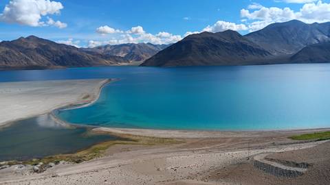 Blue lake with surrounding mountains under a clear sky.