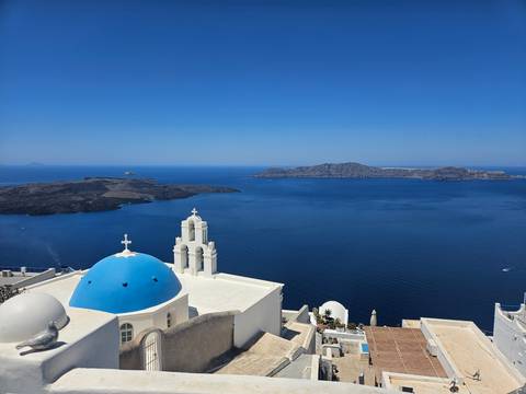 A scenic view of the sea with a blue-domed building in the foreground and rocky islands in the background.
