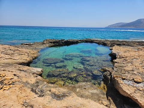 Clear blue water with a natural pool formed in rocky terrain near the ocean.