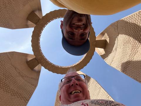 Two men taking a selfie under a circular architectural structure.