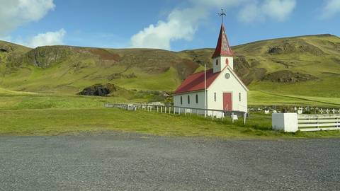 Picturesque red-roofed church amidst verdant Icelandic hills.