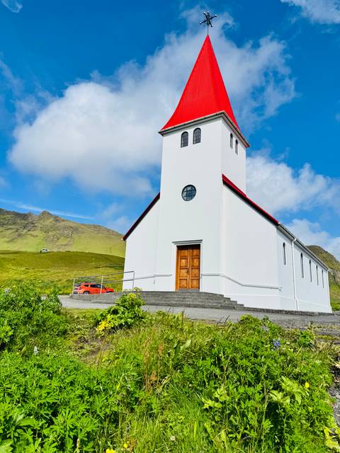 Charming white church with a red roof set against a hill.