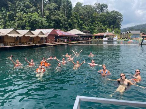 Group of people enjoying swimming in a lake with bungalows.