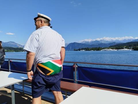 A man wearing a South African flag outfit on a boat with mountains in the background.