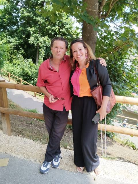 A man and a woman posing together on a sunny day with trees behind them.
