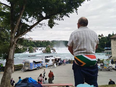 A man enjoying the view of a waterfall, standing near a river.