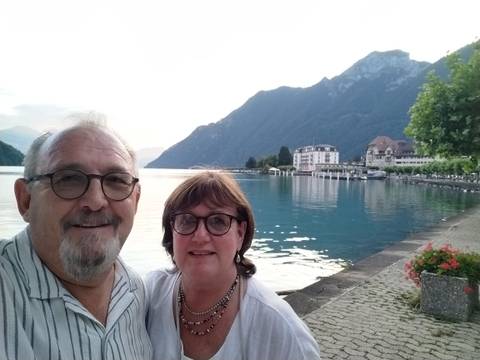 A couple standing by a lake with mountains in the background at sunset.