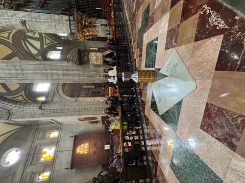 Interior of a grand cathedral with people sitting and admiring the architecture.
