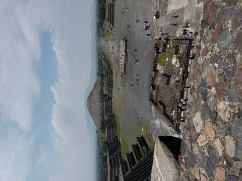 Wide-angle view of an ancient archaeological site with pyramids and tourists.