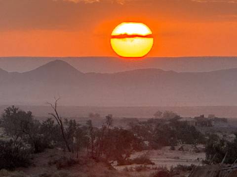 Bright orange sun setting over distant mountains and desert.