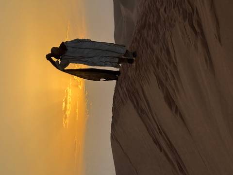 Man walking on sand dune carrying fabric.