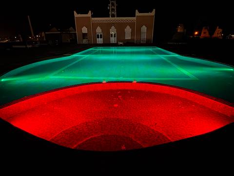 Swimming pool illuminated with red and green lights at night.