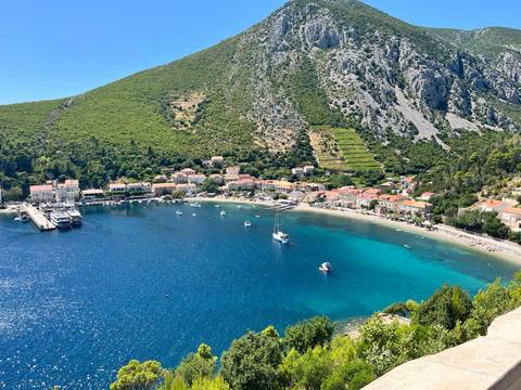 Scenic view of a coastal village with blue water and green hills.