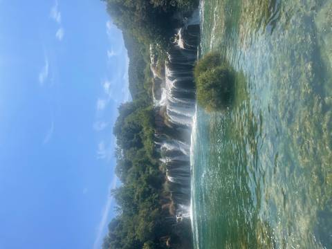 Waterfall surrounded by greenery on a sunny day.