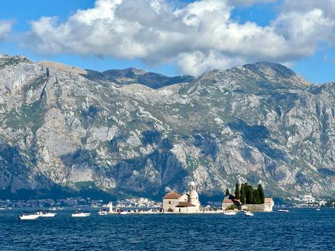 Island with a church and cypress trees on water.