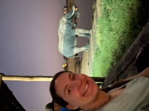 Woman taking a selfie with an elephant drinking water in the background.