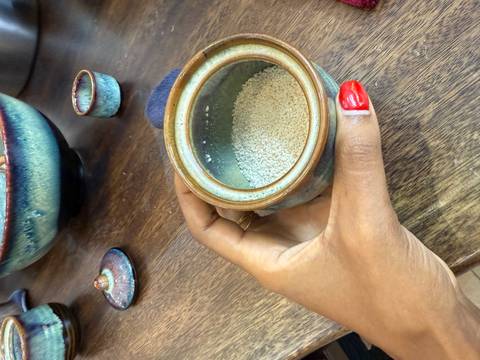 Hand holding a ceramic pot with a light green grain substance inside.