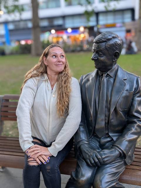 A woman sitting next to a statue of a man on a bench.