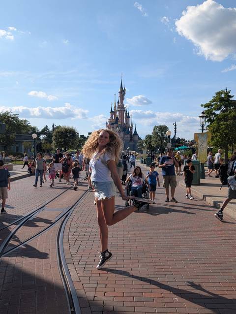 A woman joyfully posing in front of a castle-themed amusement park.
