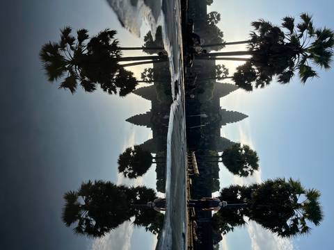 Reflection of Angkor Wat and palm trees in water during sunrise.