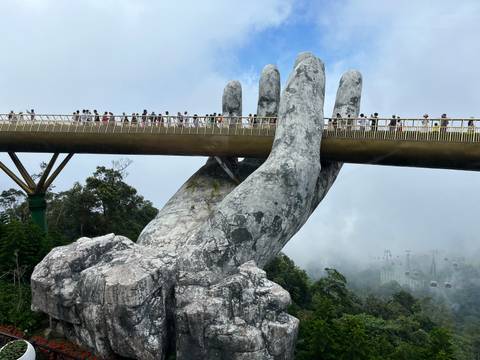 Tourists walking on the Golden Bridge supported by giant stone hands.