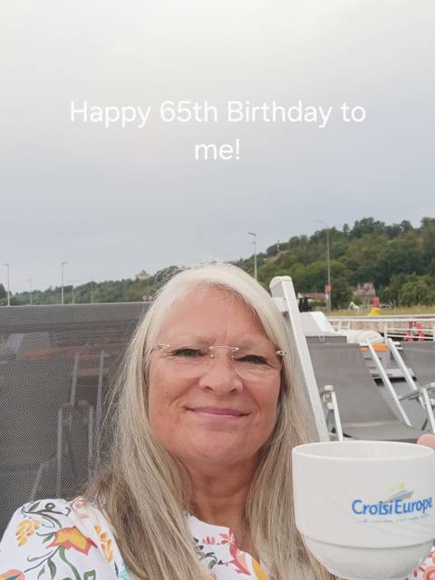 A woman smiling on a deck with a view of trees in the distance.