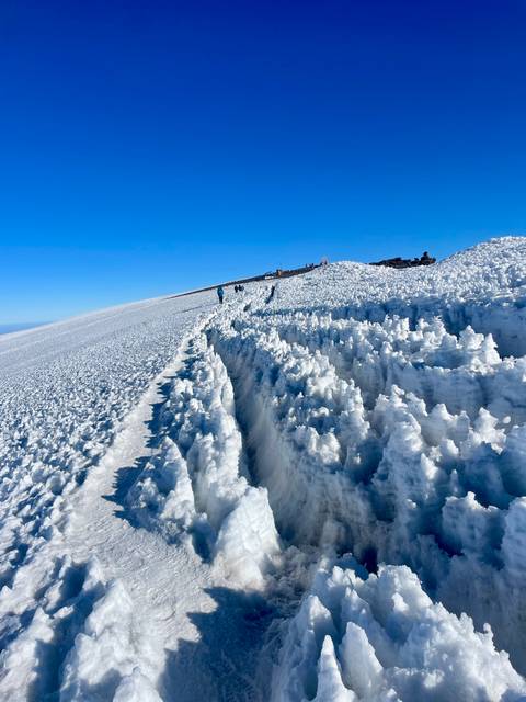 Snow-covered mountain path with climbers in the distance.