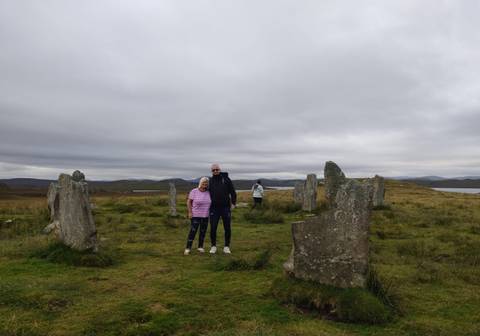 Two people posing among standing stones with grassy plains.