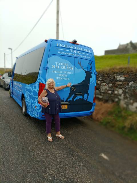 Person standing beside a blue tour bus.