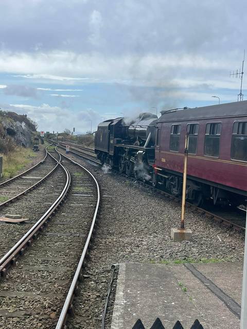 Steam train on railway tracks in a rural setting.