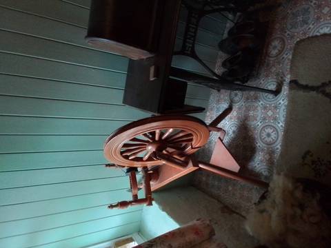Wooden spinning wheel next to an old sewing machine.