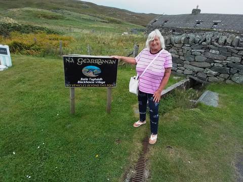 Person posing with a sign for Na Gearrannan Blackhouse Village.