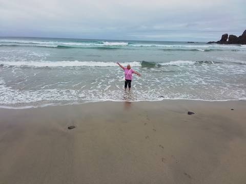 Person wading into the ocean near a sandy beach.