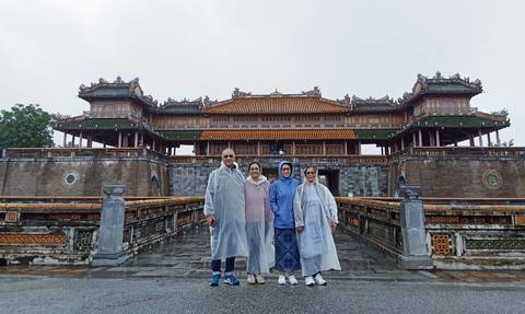 Family posing in front of an ornate East Asian building, with rain ponchos due to a rainy day.