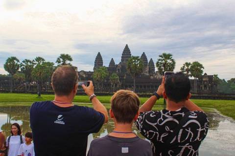 Tourists taking photos of Angkor Wat with a reflection in a pond.