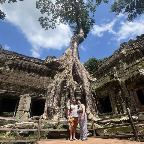 People standing near a giant tree growing over ancient temple ruins.