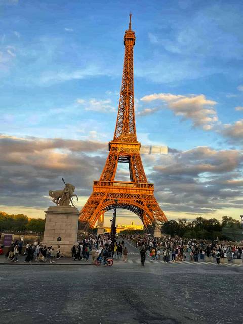 The Eiffel Tower with a statue in the foreground under a vibrant sky.