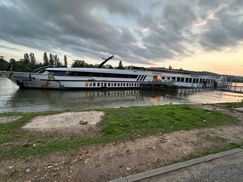 Cruise ship docked by the river with a cloudy sky.