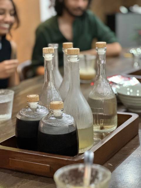 Assorted bottles on a wooden table in a cozy setting, with people in the background.