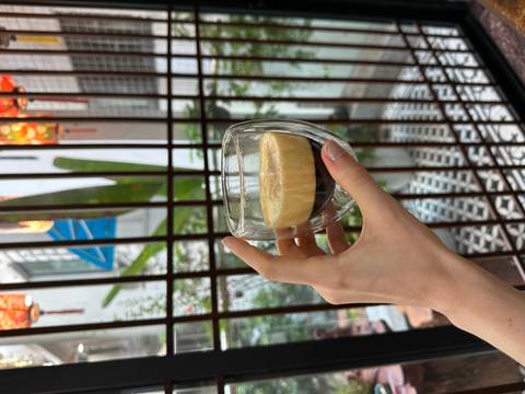 Hand holding a double wall glass filled with espresso next to a window.