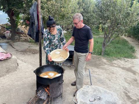 Two people cooking outdoors with large pots, surrounded by trees.
