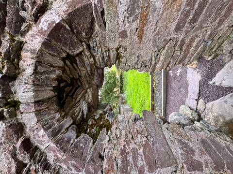 Old stone wall with archway overlooking a grassy area.