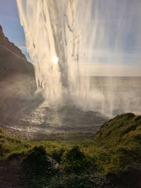 View from behind a waterfall with sunlight streaming through the water.
