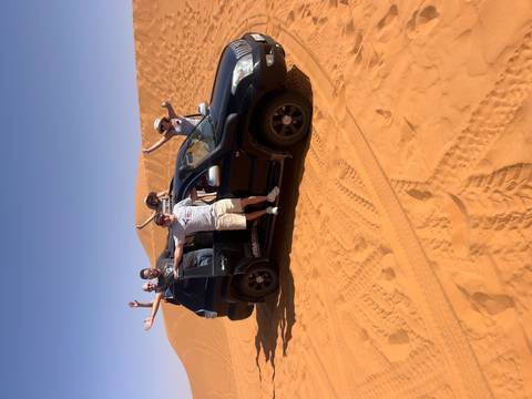 Group of people posing with an off-road vehicle in the desert.