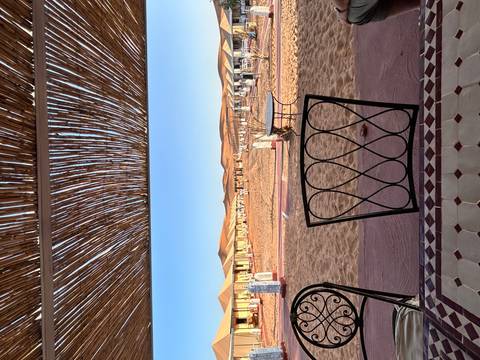 Desert camp with tents and woven roof structure.