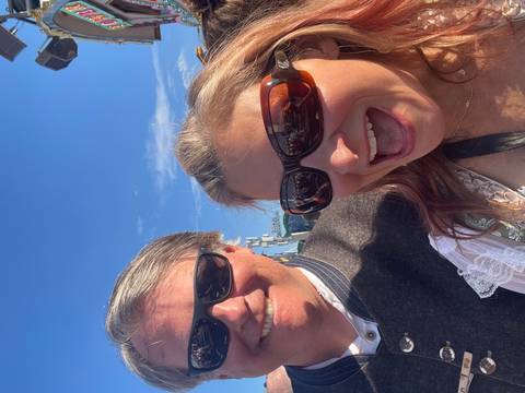 Close-up of two smiling people wearing sunglasses outdoors.