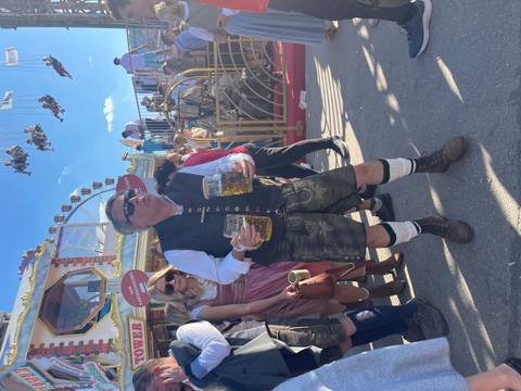 Person holding two beer steins at an outdoor festival.